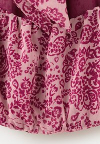Lyserødt stof med dyb magentarød blomster- og paisleymønster, med rynker og en bundet sløjfedetalje øverst.