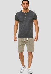 Grijze korte mouwen t-shirt met drie knopen, gecombineerd met beige shorts met twee voorzakken en een drawstring. Witte sneakers.