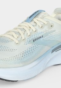Weißer und hellblauer Brooks Adrenaline GTS Laufschuh mit Mesh-Obermaterial, Schnürsenkeln und gedämpfter Sohle, seitlich in Nahaufnahme gezeigt.