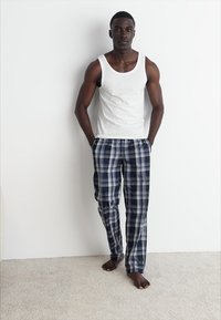 Un débardeur blanc et un pantalon de pyjama à carreaux navy avec des accents bleus et blancs. Le tissu semble doux, avec une coupe décontractée et une taille élastique.