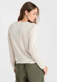 Hellbeiger Pullover mit langen Ärmeln, rundem Ausschnitt und weicher Textur. Verfügt über einen enganliegenden Saum und erscheint leicht durchsichtig.