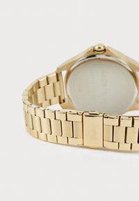 Goldfarbene Uhr mit einem Metallarmband. Verfügt über ein rundes Gehäuse, ein flaches Mineralglas und einen Klappverschluss. Glatte, reflektierende Oberfläche mit eingraviertem Logo.