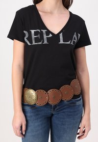Camiseta negra de cuello en V con letras plateadas que dicen "REPLAY". Cinturón de cuero marrón con acentos circulares y una gran hebilla decorativa de latón.