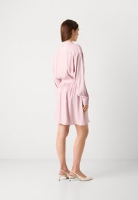 Pink short dress with long sleeves and an elastic waist. Fabric appears smooth with a relaxed fit. Worn with beige slingback shoes.