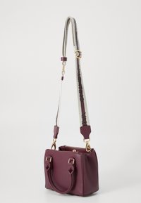 Borsa in pelle borgogna con doppie maniglie, tracolla removibile con logo, hardware dorato e chiusura con zip. Forma quadrata con design strutturato.