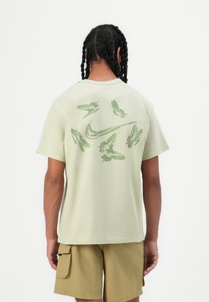 Jasnozielona bawełniana koszulka z grafiką owadów i logo Nike na plecach. Krótkie rękawy, luźny fason i okrągły dekolt.