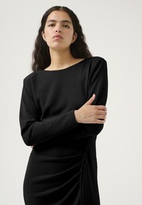Must mustaga, sujuva kangaga, millel on paadi kujuline kaelus ja volditud küljeosa, et lisada tekstuuri.