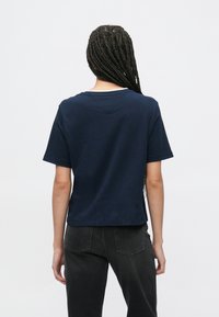 Tumesinist värvi puuvillane t-särk ümarate kaeluse ja lühikeste varrukatega. Lihtne disain sirge servaga, kantud tumedate teksapükstega.