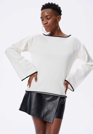 Biała sweter z czarnym wykończeniem, szerokimi rękawami, w połączeniu z czarną skórzaną mini spódnicą z ukośnym cięciem i błyszczącą teksturą.