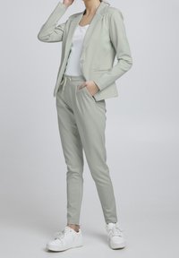 Jasnozielony komplet garniturowy z dopasowaną marynarką i spodniami z elastycznym pasem. Noszony z białą bluzką i białymi trampkami. Gładka tkanina i dopasowany krój.