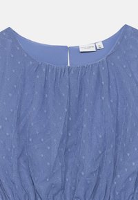Blaues Kleid mit durchscheinendem gepunktetem Overlay und gerafftem Ausschnitt, veranstaltet mit einem kleinen Schlüssellochverschluss hinten und einem Etikett im Kragen.