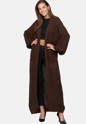 Bruine, gebreide lange cardigan met brede mouwen, twee voorzakken en een ontspannen pasvorm. Gekocht over een zwarte crop top en donkere broeken.