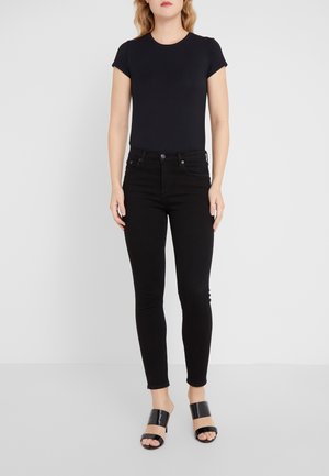 Camiseta ajustada negra, jeans slim negros y sandalias de tacón abiertas negras. Tela suave y diseño clásico; sin patrones ni acentos visibles.