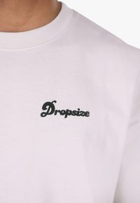 White sweatshirt featuring a round neckline and a small black "Dropsize" logo on the left chest area. Soft fabric texture.