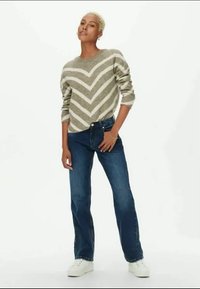 Oliivroheline kampsun valgete chevroniribadega, millele on sobitatud tumesinised teksad ja valged tossud. Istuvus on mugav.