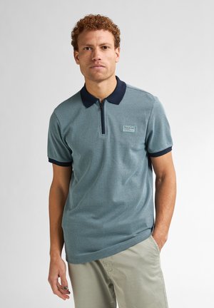 Poloshirt in Teal mit strukturiertem Muster, kontrastierendem dunklem Kragen und Ärmeln, Reißverschluss und kleinem Logo-Patch auf der Brust.
