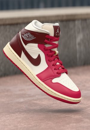 Wysokie sneakersy Air Jordan w kolorze białym, ciemnoczerwonym i różowym, wiszące nad betonową powierzchnią, pokazujące detale boczne i przednie.