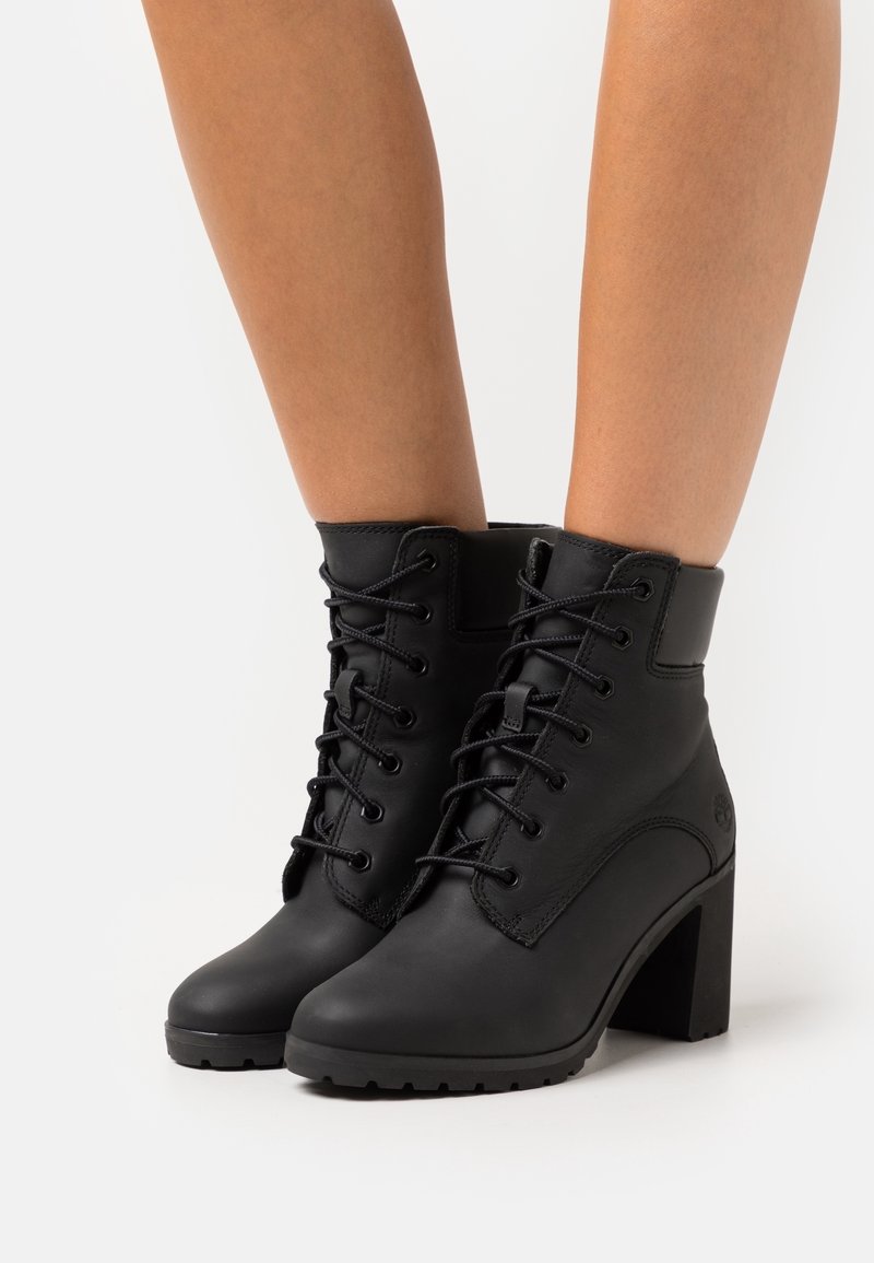 Černé kožené kotníkové boty s tkaničkami, pevnou patou a texturovanou podrážkou. Mají hladký svršek s jemným detaily švů.