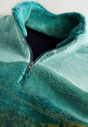 Fleecová mikina s vysokým límcem, zobrazující tyrkysový přechod a přední zip. Měkká textura s různými barevnými tóny.