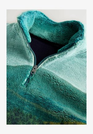 Polár pulóver magas gallérral, türkiz színátmenettel és elülső cipzárral. Puha anyag, változatos színtónusokkal.