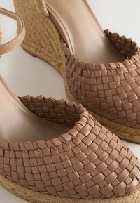 Woven taupe leather wedge sandals with a jute heel and open design, featuring a textured finish and an ankle strap closure.