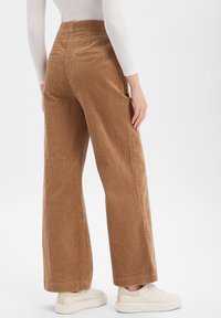 Brązowe spodnie na szerokie nogawki z sztruksu z pionowym prążkowaniem, dwoma tylnymi kieszeniami i mankietami na nogawkach. Noszone z jasnymi trampkami.