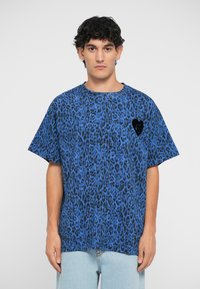 Zila leoparda raksta T-kreklā ar apaļu kakla izgriezumu, īsām piedurknēm un melnu sirds dizaina akcentu uz krūts.