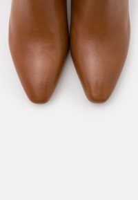 Chaussures pointues en cuir marron à texture lisse, présentant un design élégant et une forme profilée, avec des détails de couture minimaux.