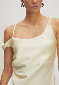 Helles gelbes Satinoberteil mit einem schulterfreien Träger, drapiertem Design und lockerer Passform, das eine Raffung im Brustbereich aufweist.