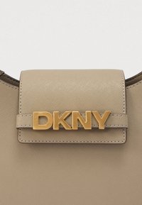 DKNY käekott beežikas sünteetilisest materjalist, millel on kuldne logoaktsent, sile tekstuur ja ristkülikukujuline klappkinnitus.