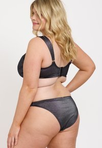 Svart, glittrande bikini med en sele-liknande bh och matchande trosor. Har breda remmar och ett spänne på baksidan för stöd.