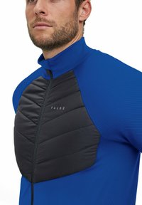 Falke jas met een felblauwe stof en een zwarte gebroken voorpaneel. Heeft een hoge kraag en ritssluiting. Gegevens met een gestructureerde stof door het hele kledingstuk.