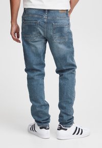Blå denimjeans med rak passform, två bakfickor, subtil blekning och en läderetikett vid midjan, kombinerade med vita sneakers.