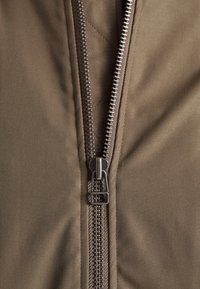 Gros plan d'une fermeture éclair métallique partiellement ouverte sur un tissu marron, montrant des coutures détaillées et l'alignement des dents de la fermeture.