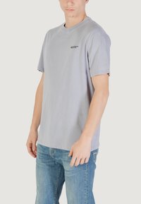 T-shirt grigio a maniche corte realizzato in morbido cotone, con un piccolo logo nero sul petto sinistro, vestibilità rilassata e taglio casual.