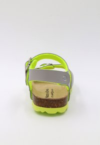 Sandale grise avec des accents néon verts vif, semelle en liège et boucle en argent ajustable. Semelle texturée offrant adhérence et confort.