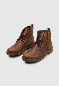 Bottines en cuir brun avec un bout rond, un laçage sur le devant et une fermeture éclair sur le côté. Présente des accents en tissu texturé au niveau du col et des côtés.