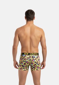 Boxer colorés vifs présentant un motif léopard en rose, noir et bleu sur un fond jaune, avec une ceinture noire.
