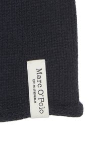 Donkerblauwe gebreide stof met een structuur aan het oppervlak. Voorzien van een wit label met "Marc O'Polo" en "EST. IN STOCKHOLM" bedrukt in zwart.