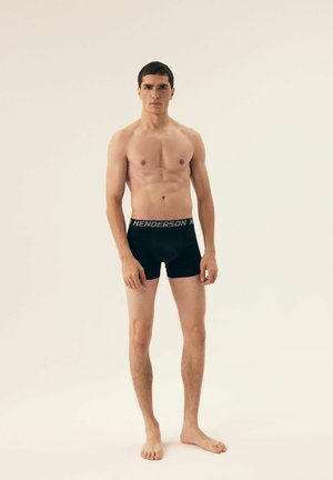 Black boxer briefs with a soft waistband featuring "HENDERSON" in silver lettering, displayed on a standing male figure.