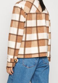 Brun och vit rutig fleecejacka med knappmanchetter, kontrasterande brun stickning och en avslappnad passform. Texturerad, varm tyg.