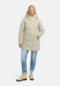 Piumino grigio chiaro con una vestibilità rilassata, cappuccio, chiusura con zip e motivo trapuntato; abbinato a jeans blu e stivali beige chiari con lacci.