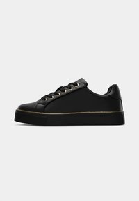 Sneaker neri con una superficie liscia, dotati di occhielli dorati, una suola nera spessa e un design a bassa altezza. Accentuati da una striscia dorata.