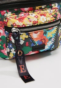 Pochette en tissu à motifs floraux avec une fermeture éclair argentée et une languette en tissu noire avec l'inscription "LOVE" en lettres multicolores.