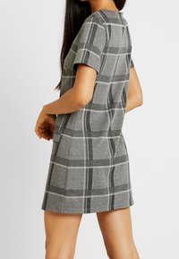 Grijze geruite jurk met korte mouwen, gemaakt van zachte stof, met een ronde halslijn en een ontspannen pasvorm, voorzien van contrasterende zwart-witte strepen.