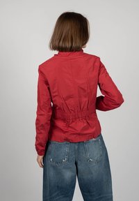 Rød, letvægt jakke med høj krave, elastisk talje og lange ærmer, der har en glat tekstur og et enkelt design. Sammen med løse jeans.