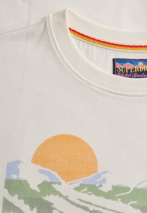 Camiseta blanca de cuello redondo con un gráfico de un sol naranja poniéndose detrás de olas verdes y azules y un detalle en el cuello con rayas multicolores.