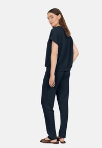 Tmavě modrá mikina s krátkým rukávem a volnějším střihem, spárovaná s odpovídajícími tepláky. Boty mají perforovaný design pro prodyšnost.