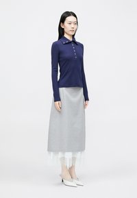 Tricou polo cu mâneci lungi, de culoare bleumarin, cu detalii cu nasturi, asortat cu o fustă gri cu tiv din dantelă și încălțat cu pantofi albi cu vârf ascuțit.