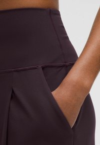 Burgundy urheiluhousut korkealla vyötäröllä, joissa on sivutasku ja sileä pinta, jota korostaa kontrastivärinen ompelu.